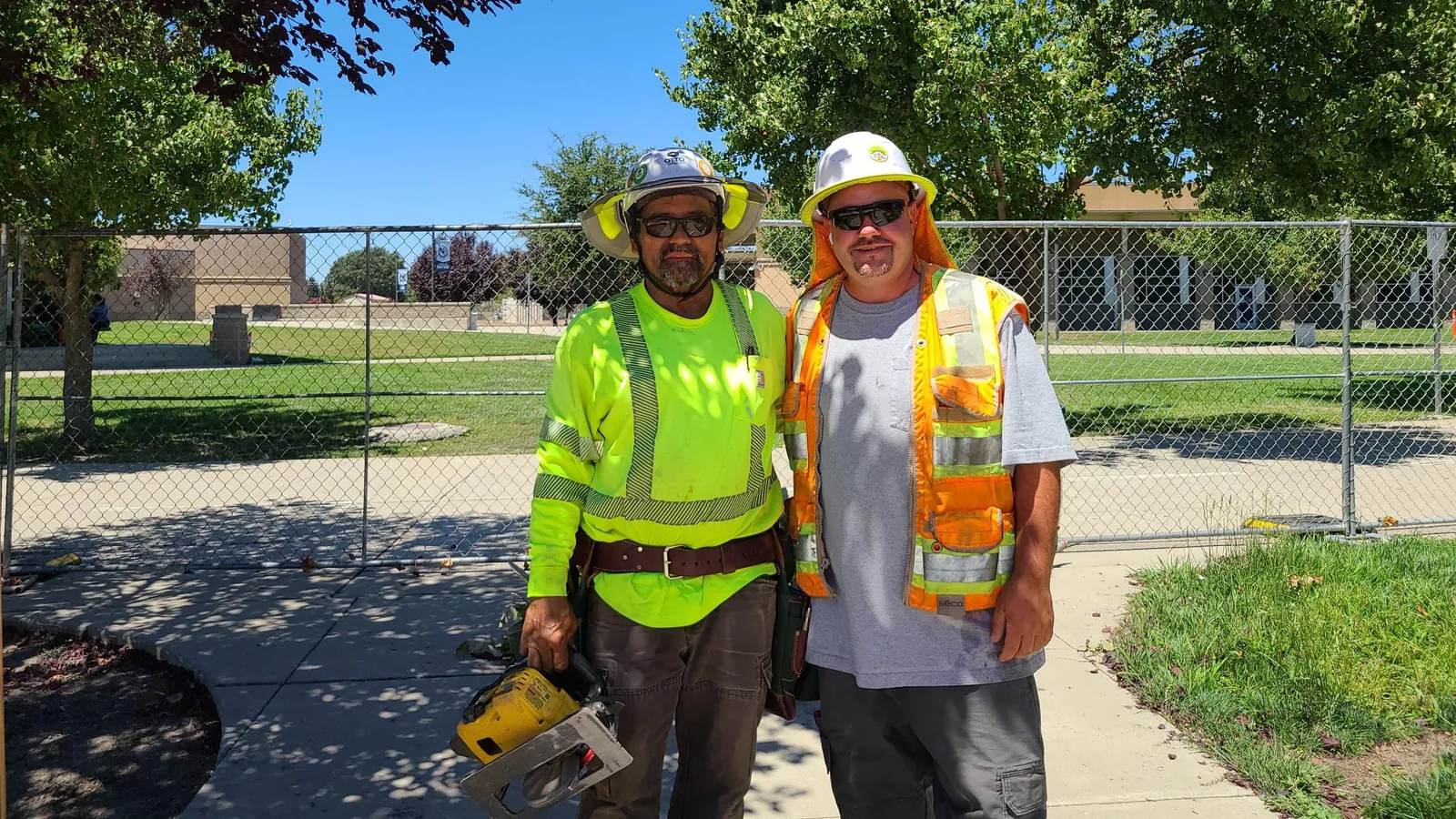Two Marina crew members in hard hats and high-visibility gear, one holding a chainsaw
